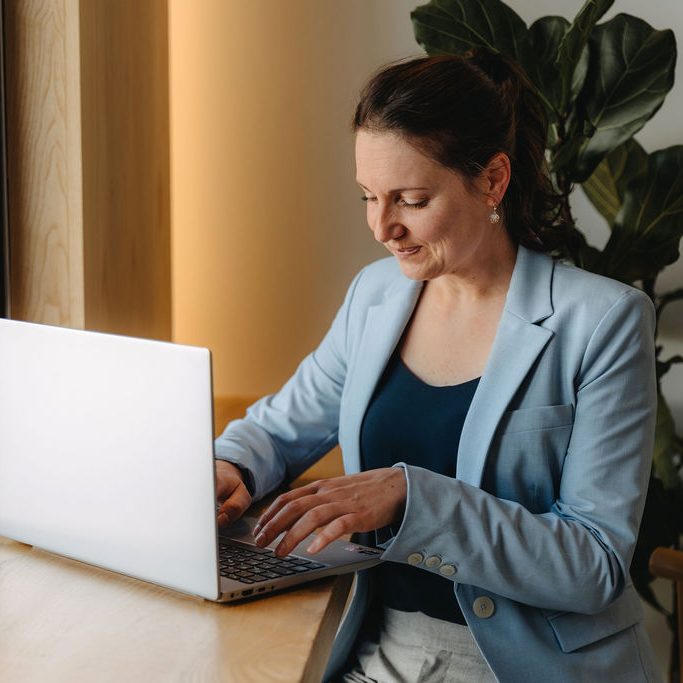 Frau sitzt an einem Tisch und arbeitet konzentriert an einem Laptop. Pflanzen im Hintergrund. Nancy Mees, die freie Traurednerin.