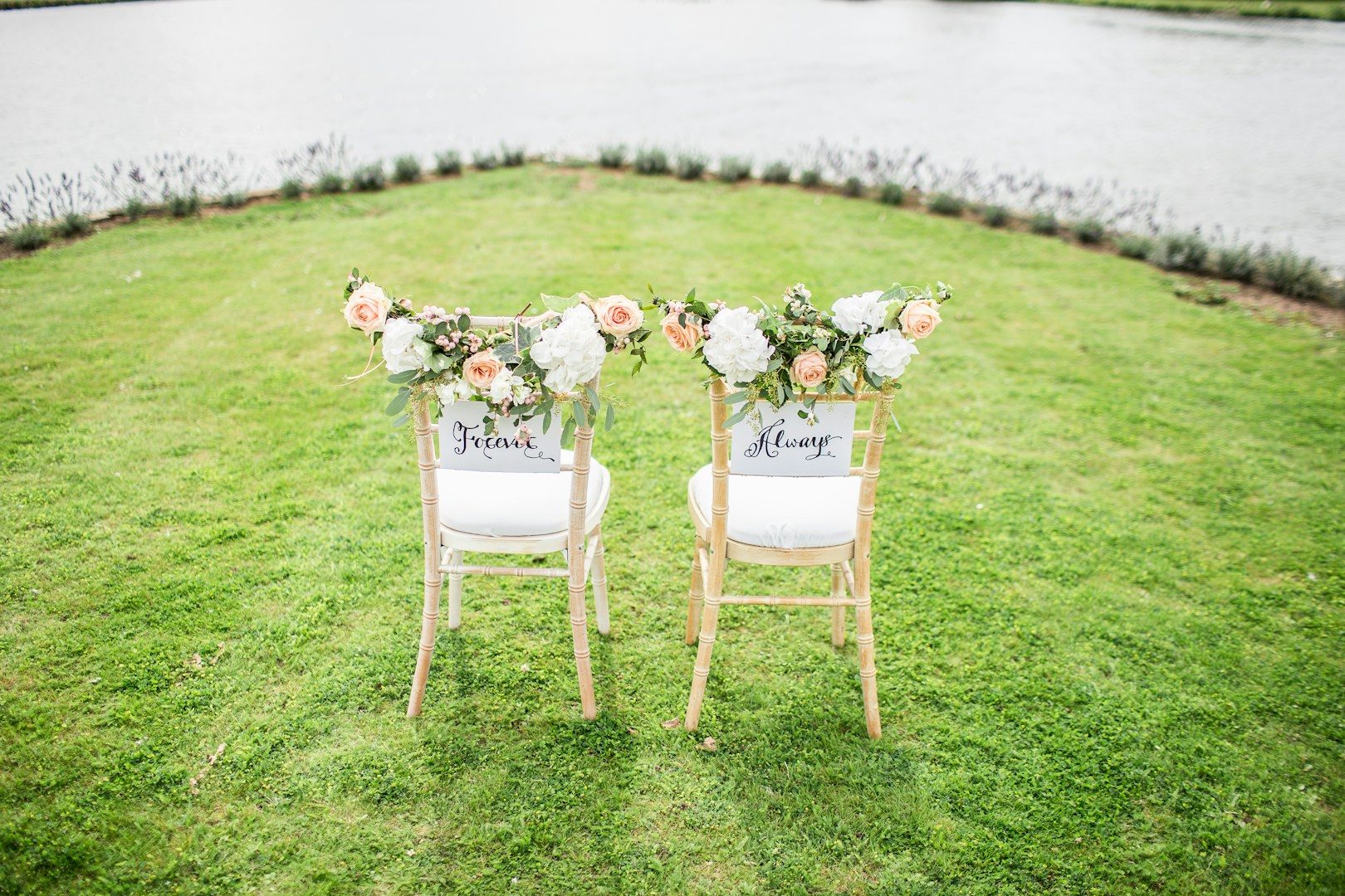Zwei dekorierte Stühle mit Blumenarrangements, Blick auf einen See.